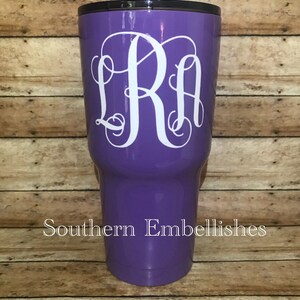 May include: Purple stainless steel tumbler with a white monogram "LRA" on the front. The tumbler is on a wooden background.