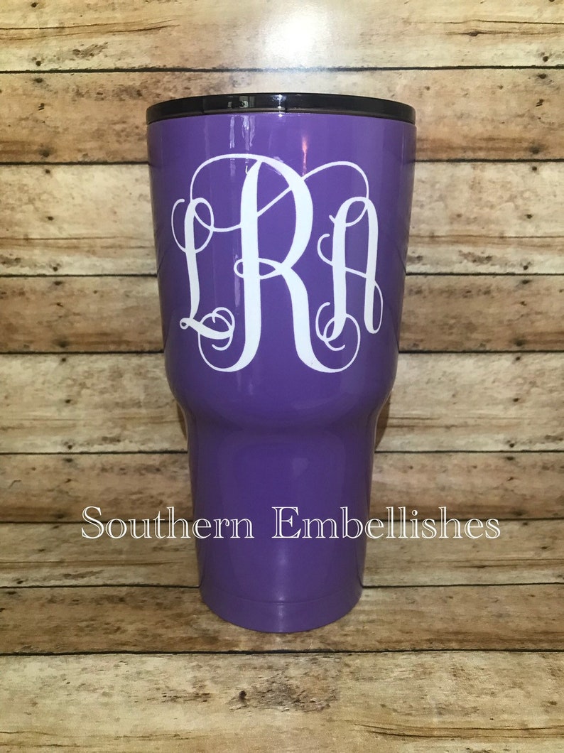 May include: Purple stainless steel tumbler with a white monogram "LRA" on the front. The tumbler is on a wooden background.