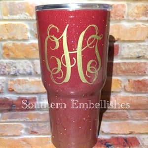 May include: A red glitter tumbler with a gold monogram "CHS" on the front. The tumbler is sitting on a brick surface. The text "Southern Embellishes" is visible below the tumbler.