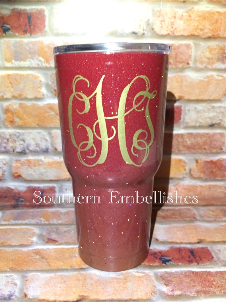 May include: A red glitter tumbler with a gold monogram "CHS" on the front. The tumbler is sitting on a brick surface. The text "Southern Embellishes" is visible below the tumbler.