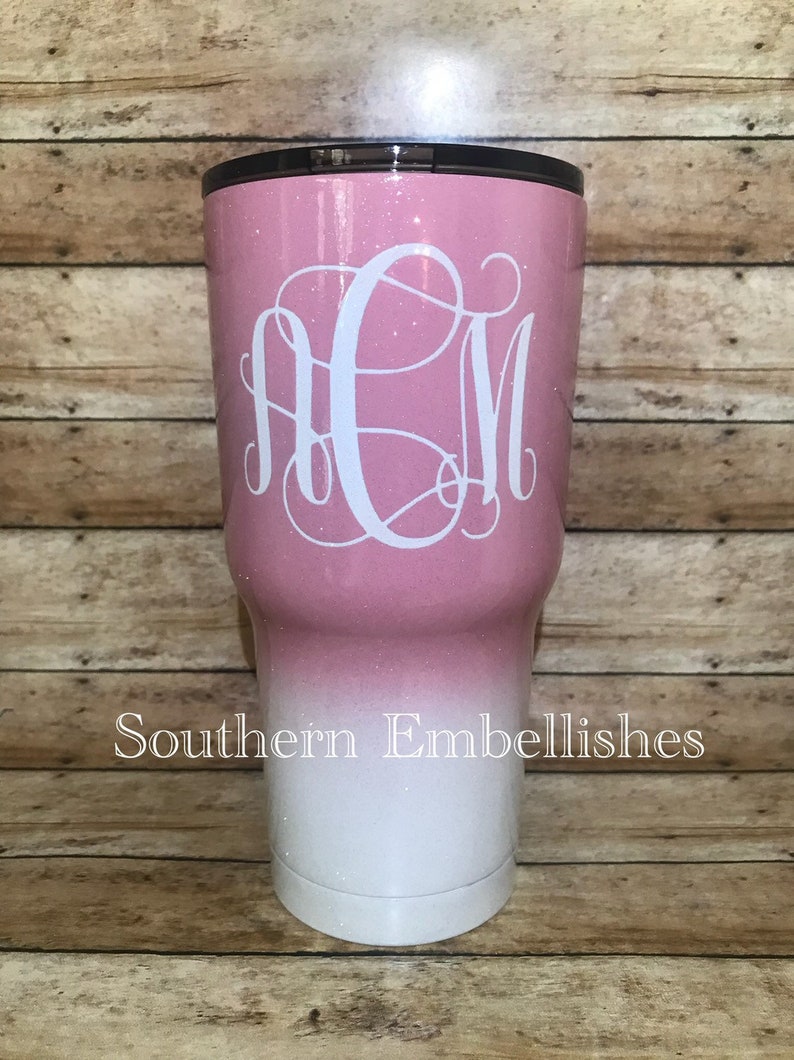 May include: A pink and white ombre glitter tumbler with a white monogram "ACM" on the front. The tumbler is made of stainless steel and has a double-wall insulated design. The text "Southern Embellishes" is printed on the bottom of the tumbler.