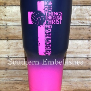 May include: A navy blue and pink tumbler with a volleyball and a cross graphic. The tumbler has the text "I can do all things through Christ who strengthens me".