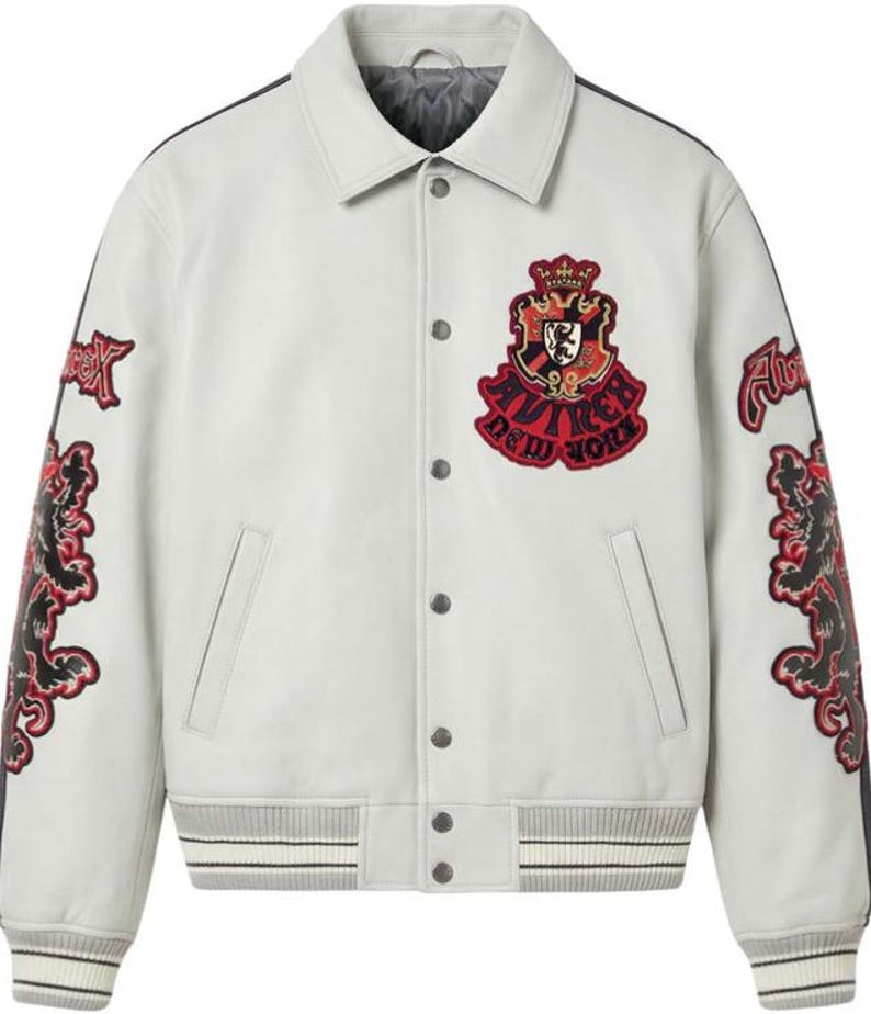 Puede incluir: Chaqueta universitaria gris claro con parches bordados en negro y rojo. La chaqueta tiene una parte delantera abotonada, un cuello y pu&ntilde;os y dobladillo acanalados con rayas blancas. Los parches incluyen un escudo y el texto "Avirex New York".