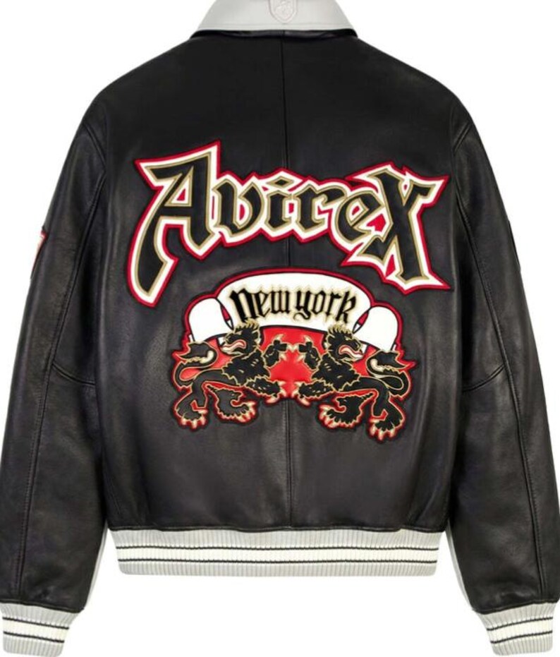 Puede incluir: Chaqueta de cuero negra con cuello y pu&ntilde;os blancos. La espalda presenta un gran dise&ntilde;o bordado con la palabra "Avirex" en rojo y dorado, y "New York" en una pancarta. Debajo, dos figuras de leones.