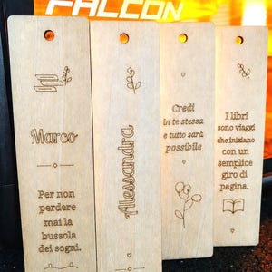 Può includere: Quattro segnalibri rettangolari in legno chiaro con angoli arrotondati e un foro in alto. Ognuno presenta testi in italiano incisi al laser, motivi floreali e piccoli cuori. I design includono nomi, citazioni ispiratrici e la data 15.05.2024.
