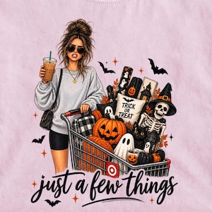 May include: A light pink t-shirt featuring a graphic of a person with sunglasses holding a coffee, pushing a shopping cart filled with Halloween items including a pumpkin, a skeleton, and a pillow with the text Trick or Treat and just a few things.