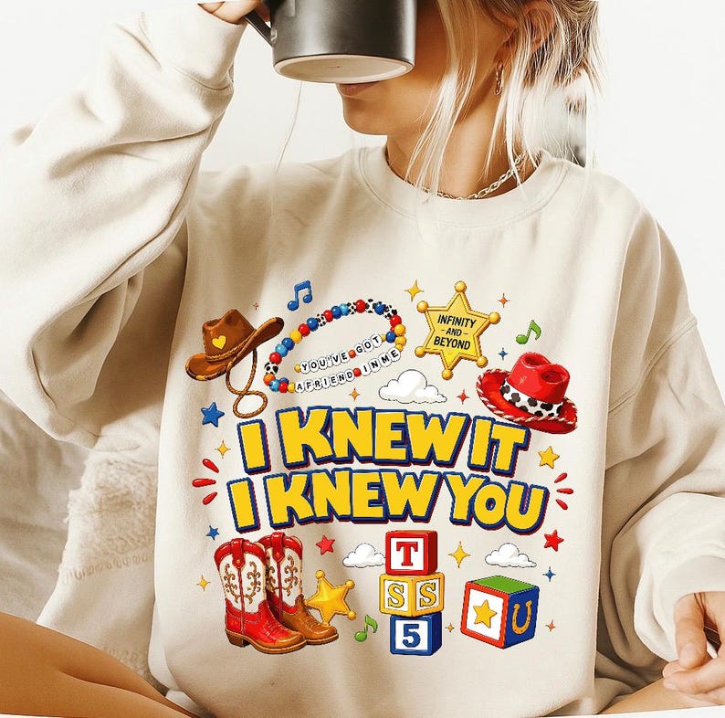 May include: A beige crewneck sweatshirt featuring a graphic print with a brown cowboy hat, a red cowgirl hat, a beaded bracelet with the text YOU'VE GOT A FRIEND IN ME, a yellow sheriff star, alphabet blocks, and the text I KNEW IT I KNEW YOU.