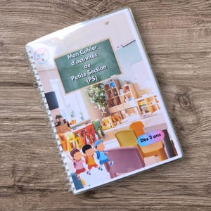 Peut inclure: Un cahier d'activités à reliure spirale intitulé Mon Cahier d'activités de Petite Section (PS) illustré d'une salle de classe avec un tableau, des étagères en bois, des chaises colorées et trois enfants. Une étiquette rose indique Dès 3 ans.