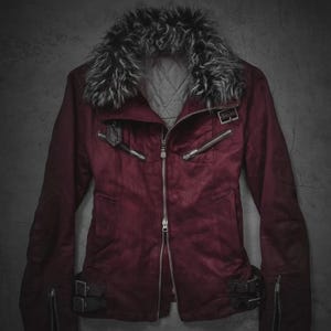 Könnte beinhalten: Burgunderfarbene Jacke mit Kunstfellkragen. Die Jacke hat einen Reißverschluss, mehrere Reißverschlusstaschen und Schnallendetails an den Ärmeln und der Taille. Das Futter ist gesteppt.