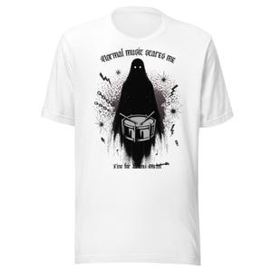 Peut inclure: T-shirt blanc avec un motif noir d'une figure encapuchonnée jouant de la batterie. Le texte "Normal music scares me" est au-dessus de la figure, et "Time for drum metal" est en dessous. Le motif comprend des éclairs et des éclats d'étoiles.