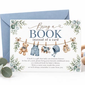 May include: A rectangular card with a blue envelope featuring the text Bring a BOOK instead of a card. The design includes watercolor illustrations of a teddy bear, overalls, a toy airplane, a bonnet, and booties hanging on a clothesline.