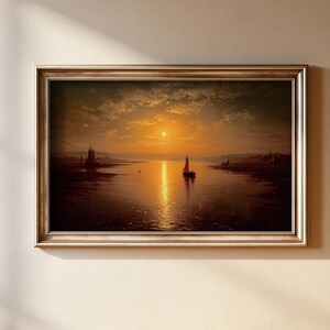 May include: A framed landscape painting depicting a sunset over a calm body of water with two sailboats silhouetted against the golden light. The scene features a dark, reflective surface of the water and a cloudy sky in shades of orange and brown.