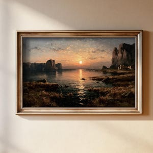 May include: A landscape painting in a metallic gold frame depicting a sunset over a calm body of water. The scene features dark rocky cliffs on both sides, a bright sun low on the horizon, and a grassy shoreline in the foreground with warm light.