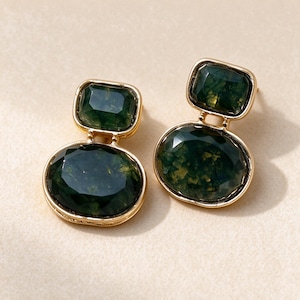 May include: A pair of gold-tone drop earrings featuring two faceted, dark green moss agate stones each. The top stone is rectangular with rounded corners, while the bottom stone is oval. Both stones are set in polished gold-tone metal frames.