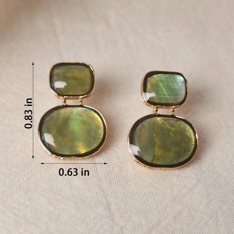 May include: A pair of gold-tone earrings featuring two stacked, iridescent green shell-like stones in a rectangular and oval shape. The earrings measure 0.83 inches in height and 0.63 inches in width as indicated by the visible dimension markers.