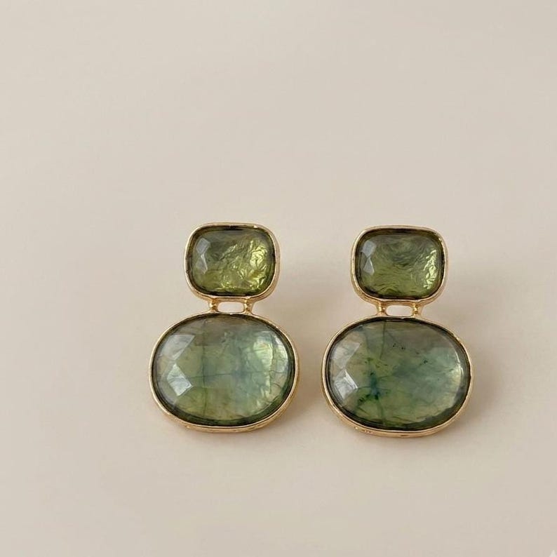 Pair of handmade drop earrings featuring rectangular and oval green stones with a Gold-Tone finish, displayed on soft white fabric.