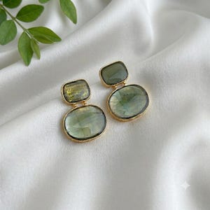 Green stone drop earrings with Gold-Tone accents resting on draped white silk, highlighting the natural translucency of the stones.