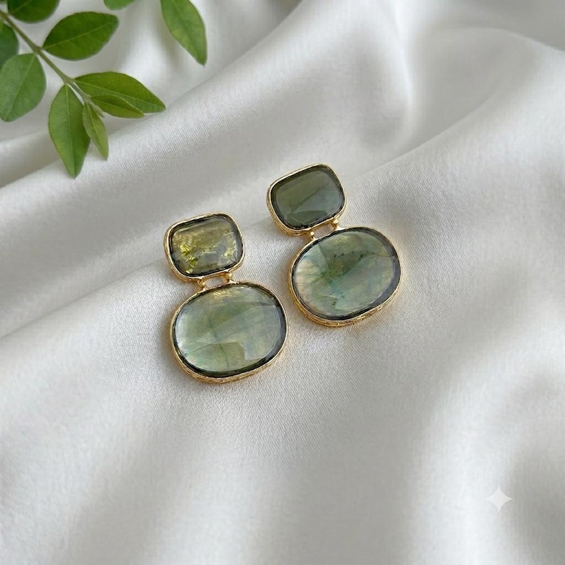 Green stone drop earrings with Gold-Tone accents resting on draped white silk, highlighting the natural translucency of the stones.