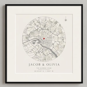 Peut inclure: Une impression de carte circulaire encadrée présentant des lignes de rues noires sur un fond crème avec une petite icône de cœur rouge au centre. Sous la carte, le texte indique JACOB & OLIVIA, THE QUEENS HEAD et les coordonnées 52.9540 N, 1.1550 W.