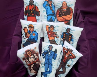 Puede incluir: Una colección de nueve cojines rectangulares de peluche con coloridas ilustraciones de dibujos animados de personajes del videojuego Team Fortress 2, incluyendo a Pyro, Soldier, Heavy, Engineer, Scout, Demoman, Medic, Spy y Sniper.