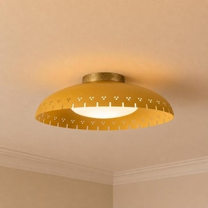May include: A yellow, mid-century modern flush mount ceiling light. The light fixture has a perforated shade with a white, frosted glass diffuser. The base is a brass color. The light is mounted on a white ceiling.