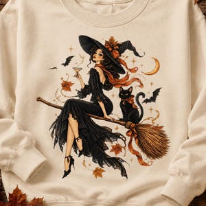 May include: A cream-colored crewneck sweatshirt featuring a graphic illustration of a witch in a black dress and pointed hat sitting on a broomstick with a black cat. The design includes orange autumn leaves, bats, and a crescent moon.