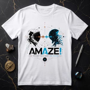 Op de afbeelding: Een wit t-shirt met korte mouwen en een grafische print van een astronautenhelm tegenover een blauw buitenaards wezen. Het ontwerp bevat geometrische lijnen, een geluidsgolf en de tekst "AMAZE! PROJECT HAIL MARY FAN DESIGN" in zwart en blauw.