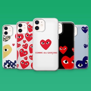 Op de afbeelding: Een verzameling telefoonhoesjes met verschillende ontwerpen. De hoesjes hebben een witte hoes met een rood hart en de tekst "Comme des Gar&ccedil;ons", een zwarte hoes met rode harten en hoesjes met hartpatronen in rood, blauw en geel.