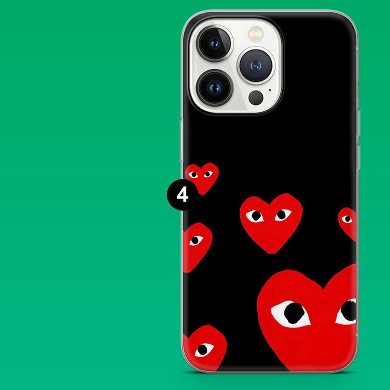 Op de afbeelding: Zwarte telefoonhoes met een patroon van rode harten met witte ogen. De hoes heeft een transparante rand en wordt getoond tegen een groene achtergrond. De telefoonhoes is ontworpen voor een smartphone.