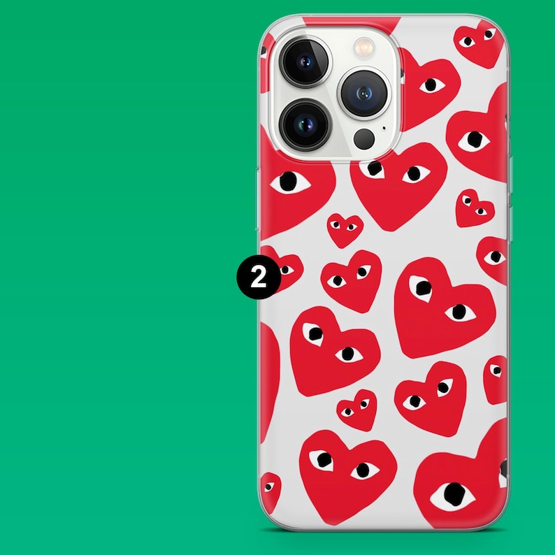 Op de afbeelding: Een doorzichtige telefoonhoes met een patroon van rode harten met zwarte ogen op een witte achtergrond. De hoes is ontworpen voor een smartphone, met uitsparingen voor de camera en andere functies. Het nummer "2" staat op de hoes.