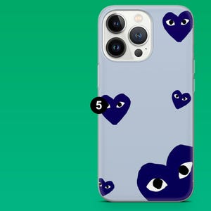 Op de afbeelding: Een lichtblauwe telefoonhoes met een patroon van marineblauwe hartvormige ogen. De hoes heeft een camera-uitsparing en een zwarte cirkel met het nummer 5.