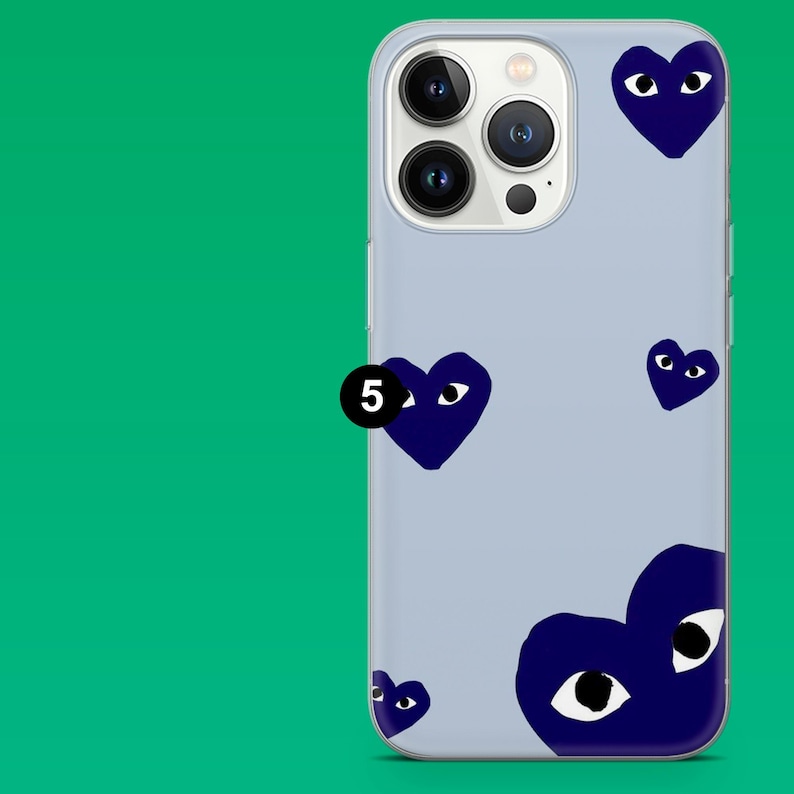 Op de afbeelding: Een lichtblauwe telefoonhoes met een patroon van marineblauwe hartvormige ogen. De hoes heeft een camera-uitsparing en een zwarte cirkel met het nummer 5.