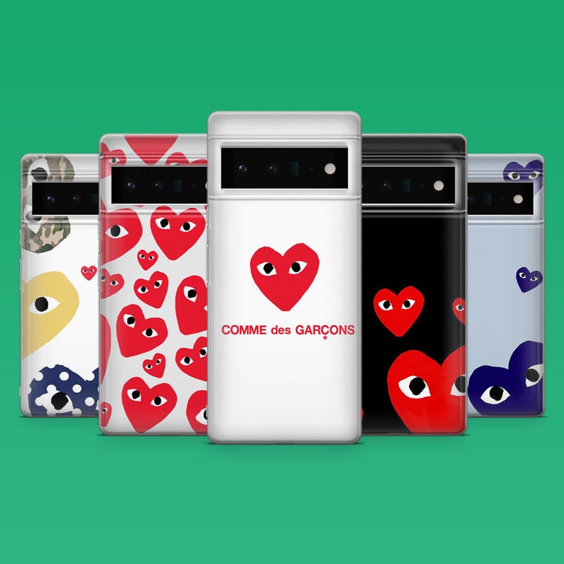 Op de afbeelding: Een verzameling telefoonhoesjes met diverse ontwerpen. E&eacute;n hoesje is wit met een rood hart en de tekst "Comme des Gar&ccedil;ons". Andere hoesjes hebben herhaalde hartpatronen, camouflage en een zwart hoesje met een rood hart. De hoesjes staan tegen een groene achtergrond.