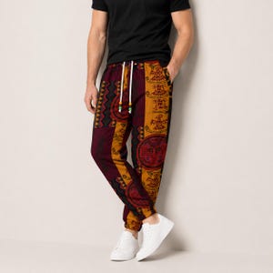 May include: Jogger pants featuring a vertical panel design with alternating maroon and mustard yellow sections. The fabric displays intricate geometric patterns and stylized bird motifs. The pants include a white drawstring with colorful beads.