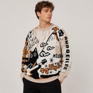 Könnte beinhalten: Ein beigefarbener Langarmpullover mit Rundhalsausschnitt, der eine schwarze Katze beim Gitarrespielen, einen Vulkan und verschiedene grafische Elemente zeigt, darunter den Text I'M A GENIVS, MEOW und japanische Schriftzeichen in Schwarz und Orange.