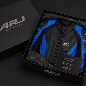 May include: A black and blue leather motorcycle jacket with a mandarin collar and front zipper, presented in a black branded gift box. The box includes branded tissue paper, a hanging tag, and a card that reads Thank You For Choosing ARJ.