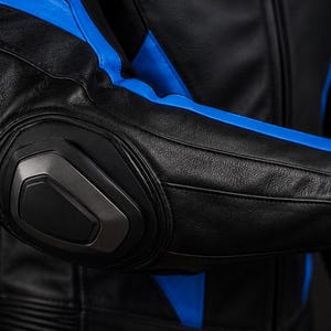 May include: A black leather motorcycle jacket featuring vibrant blue panels along the sleeves and torso. The elbow area is reinforced with a prominent, molded dark gray protective armor piece, and the sleeve cuff includes a black strap detail.