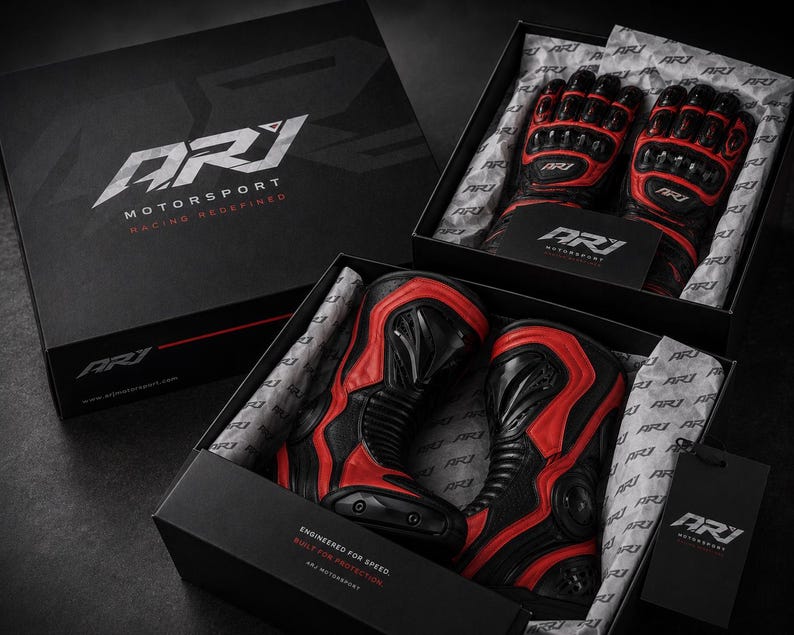 K&ouml;nnte beinhalten: Ein Paar schwarz-rote Motorradhandschuhe und ein Paar schwarz-rote Motorradstiefel in gebrandeten ARJ Motorsport-Boxen. Die Verpackung zeigt das ARJ Motorsport-Logo sowie die Texte Racing Redefined und Engineered for Speed.
