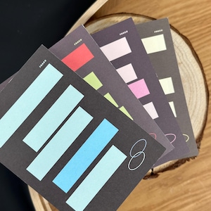 Könnte beinhalten: Ein Stapel farbenfroher Karten mit geometrischen Designs. Jede Karte hat einen dunklen Hintergrund mit rechteckigen Formen in verschiedenen Farben, darunter Blau, Rosa und Rot. Das Wort "FARGO" ist auf jeder Karte aufgedruckt. Die Zahl "8" ist ebenfalls sichtbar.
