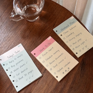 Könnte beinhalten: Drei rechteckige Aufgaben-Notizblöcke mit Lochungen an der linken Seite. Die Blöcke haben Überschriften wie Today's Tasks, Work To-Do und Weekend Plans sowie gedruckte Kästchen und handschriftlich wirkenden Text für tägliche Aktivitäten.
