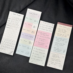 Könnte beinhalten: Eine Sammlung von vier farbigen Haftnotizblöcken. Einer ist ein Gewohnheitstracker, ein anderer eine Wochenaufzeichnung, eine To-Do-Liste und ein Brain Dump. Jeder Block hat handgeschriebenen Text und kleine Illustrationen.