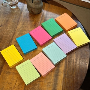 Puede incluir: Una colección de diez blocs de notas adhesivas rectangulares en varios colores neón y pastel, incluyendo amarillo, azul, rosa, verde, naranja y lavanda. Cada bloc presenta un encabezado impreso con la palabra Date y diseños de papel rayado o cuadriculado.