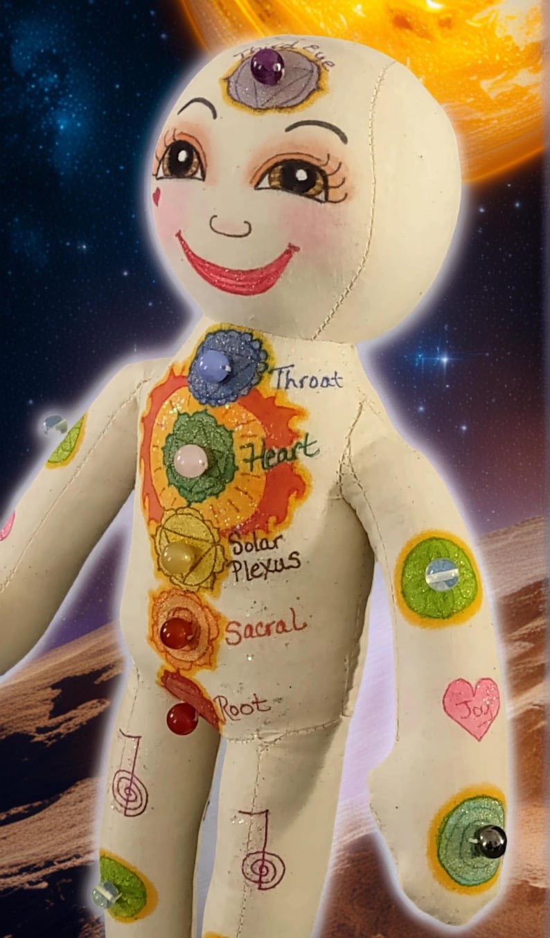 K&ouml;nnte beinhalten: Handgefertigte Puppe mit l&auml;chelndem Gesicht und bemalten Chakra-Symbolen auf dem Torso. Die Puppe hat ein drittes Auge und verschiedene Edelsteinakzente. Der Hintergrund zeigt eine kosmische Szene mit einem Planeten und Sternen.
