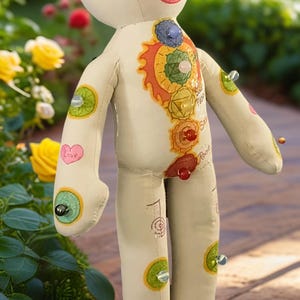 K&ouml;nnte beinhalten: Handgefertigte Stoffpuppe mit bemaltem Gesicht und K&ouml;rper. Die Puppe zeigt farbenfrohe Chakra-Symbole und Edelsteinakzente. Die Puppe hat ein l&auml;chelndes Gesicht, und das Wort "Love" ist auf einem Arm geschrieben.