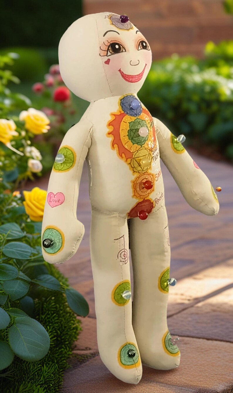 K&ouml;nnte beinhalten: Handgefertigte Stoffpuppe mit bemaltem Gesicht und K&ouml;rper. Die Puppe zeigt farbenfrohe Chakra-Symbole und Edelsteinakzente. Die Puppe hat ein l&auml;chelndes Gesicht, und das Wort "Love" ist auf einem Arm geschrieben.