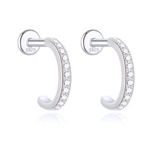 May include: A pair of silver-toned stud earrings featuring a curved, semi-circular design encrusted with small, clear, sparkling stones along the front edge. Each earring has a flat circular backing clearly stamped with the text S925.