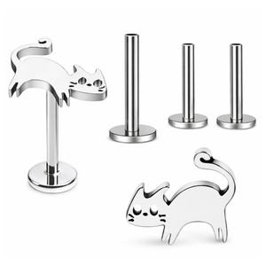 May include: A set of silver-toned metal body jewelry pieces, including two flat-back labret studs with cat-shaped tops featuring cut-out eyes and whiskers, and three plain cylindrical posts with circular bases for secure piercing attachment.
