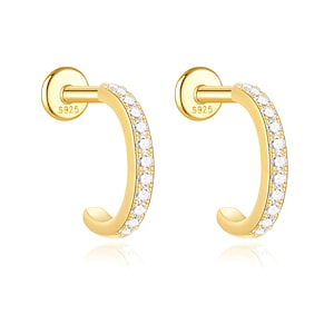 May include: A pair of gold-tone hoop earrings featuring a flat back post with the engraving S925. Each curved hoop is adorned with a row of small, clear, round-cut stones along the front edge, creating a bright, reflective, and metallic appearance.