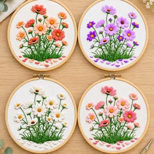 Può includere: Quattro telai da ricamo circolari in legno contenenti tessuto bianco con disegni floreali cuciti. Ogni telaio presenta un gruppo di fiori nelle tonalità arancione, viola, bianco o rosa, con steli verdi e petali sparsi alla base.
