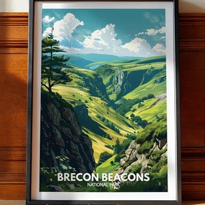 May include: A framed art print featuring a landscape illustration of the Brecon Beacons National Park. The image displays green rolling hills, rocky cliffs, a single tall tree, and a blue sky with white clouds. The text reads BRECON BEACONS NATIONAL PARK.